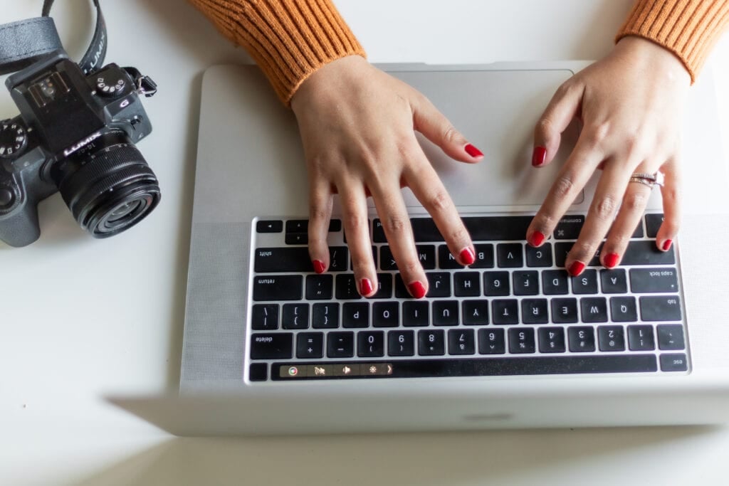 woman typing on laptop with camera in background for article about How do I start selling short stories